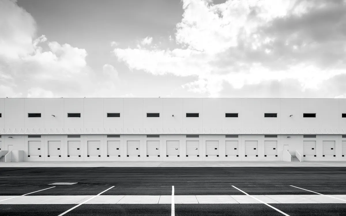 A long modern warehouse with a row of loading doors, in black and white