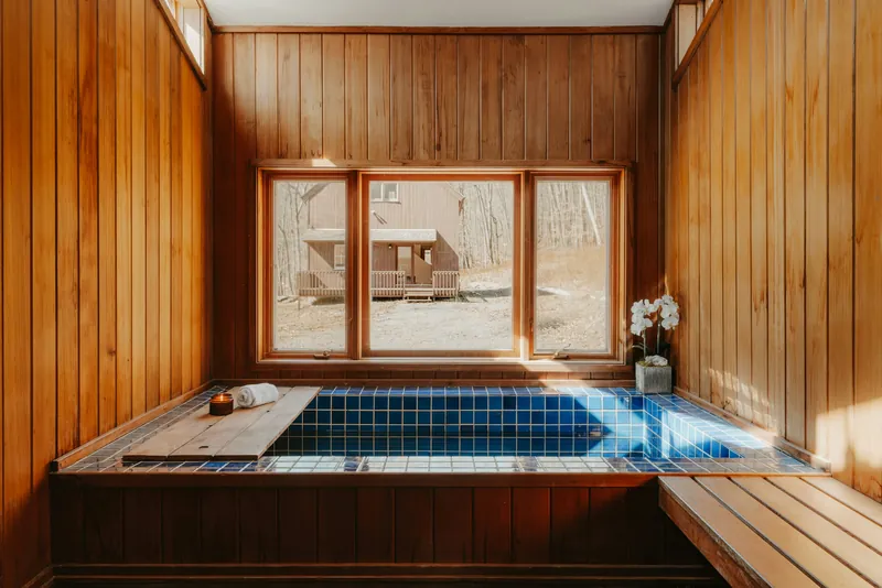 A tiled hot tub in a timber room with a large window